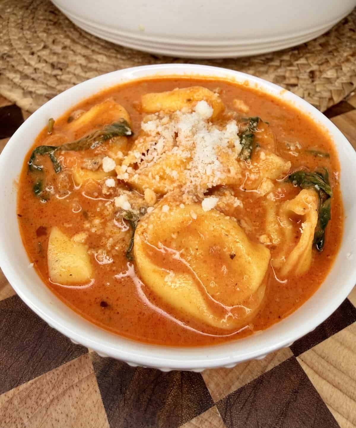 A bowl of tortellini soup with spinach and grated cheese.