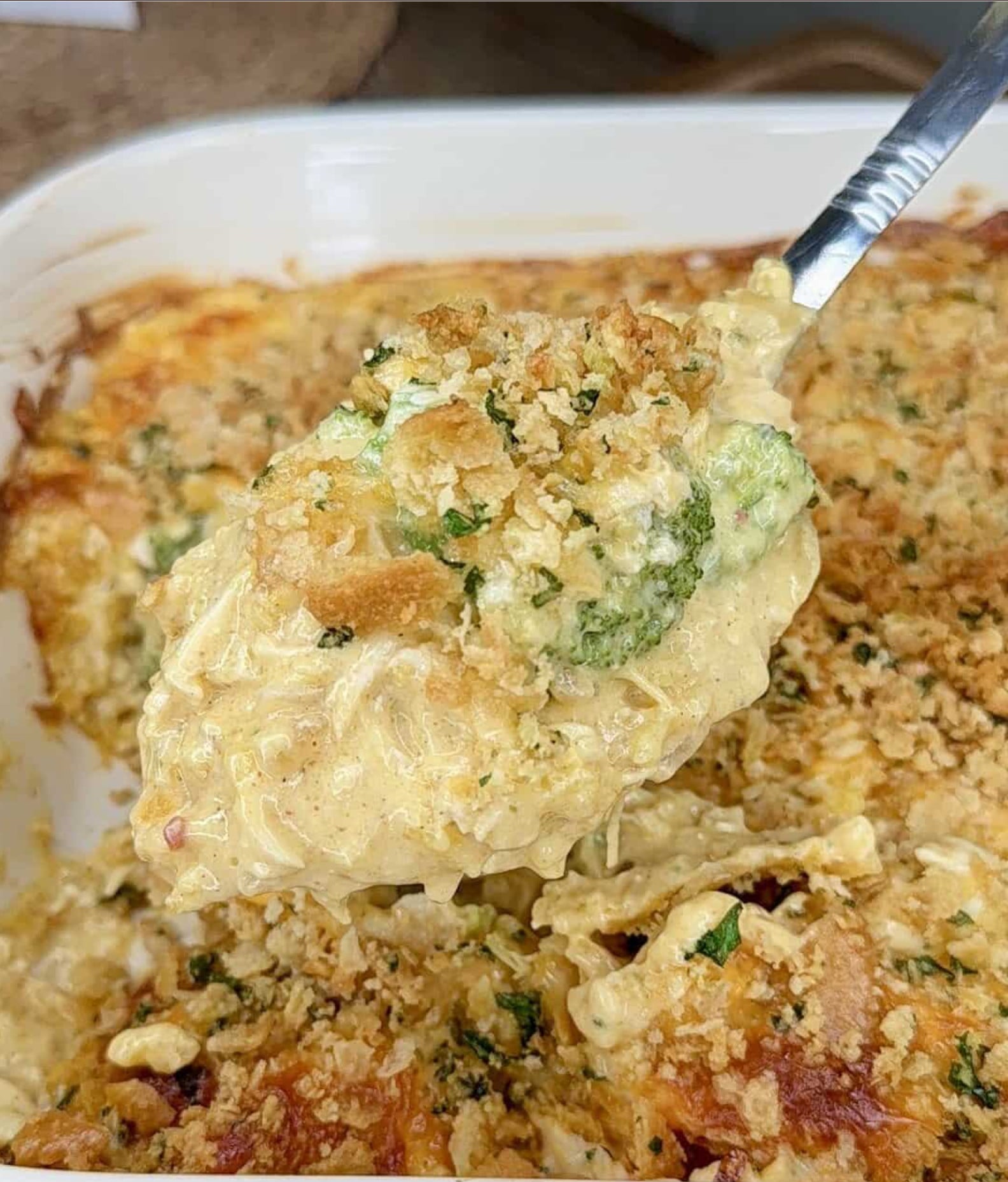 A spoonful of creamy chicken and broccoli casserole topped with breadcrumbs, lifted from a baking dish.