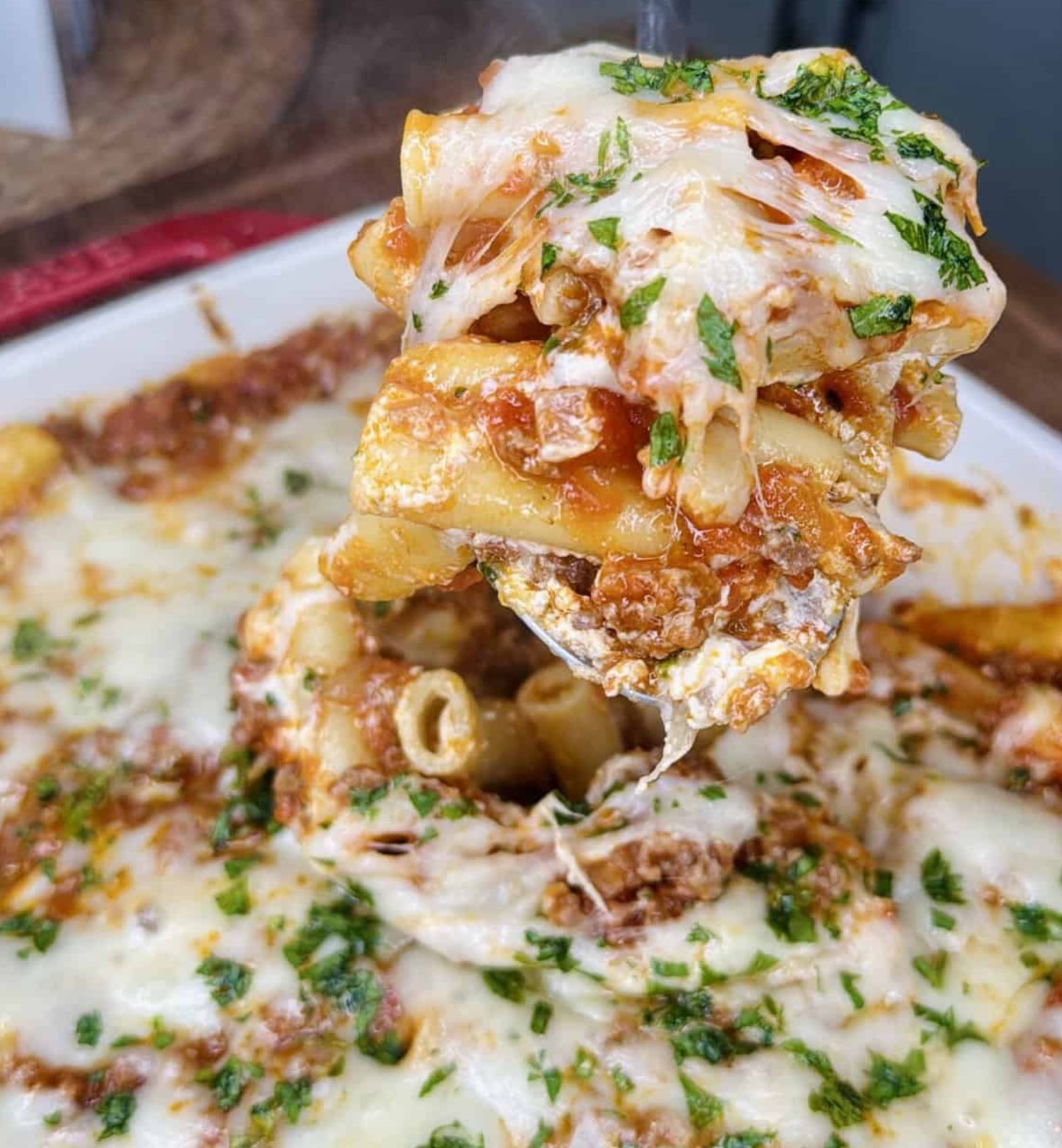 A spoonful of baked ziti with meat sauce and melted cheese being lifted from a casserole dish.