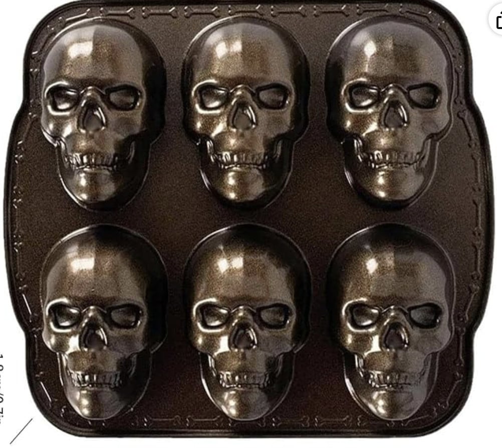 A metallic baking pan with six skull-shaped cavities.