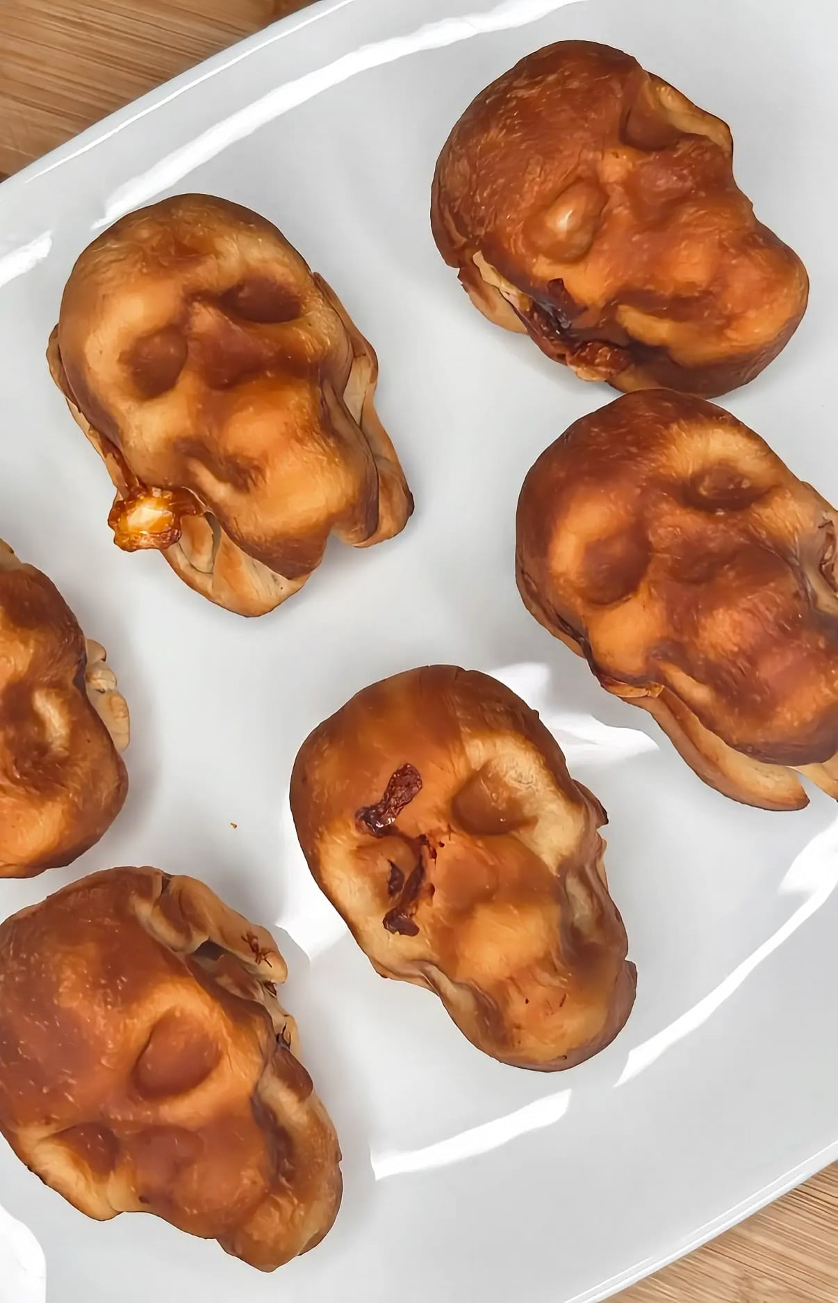 Six baked bread rolls shaped like human skulls arranged on a white plate.